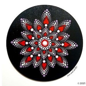 Puede incluir: Un mandala rojo y blanco con un diseño de corazón sobre un fondo negro. El mandala está hecho de puntos y está rodeado por un círculo negro.