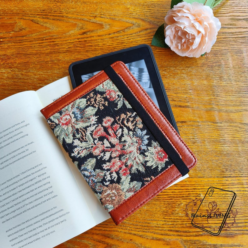 Peut inclure: Une couverture de carnet en cuir marron avec un motif de tapisserie florale noir et color&eacute;. La couverture est dot&eacute;e d'une fermeture &agrave; bande &eacute;lastique noire.
