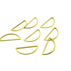 May include: A group of ten gold-colored metal half-circle shapes, each with a flat, open edge. The shapes are scattered on a white surface.
