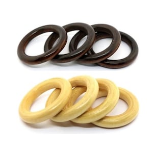 Puede incluir: Cinco anillos de madera, dos marrones y tres de color madera natural, apilados uno encima del otro. Los anillos son lisos y tienen un acabado pulido.