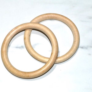 May include: Two wooden rings, one slightly larger than the other, are interlocked. The rings are a light brown color and have a smooth, polished finish.