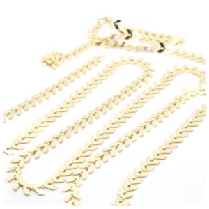 Könnte beinhalten: Goldkette mit Chevron-Muster. Die Kette besteht aus kleinen, miteinander verbundenen pfeilförmigen Teilen.
