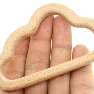 Puede incluir: Un anillo de dentici&oacute;n de madera natural con forma de nube. El anillo es liso y tiene un borde redondeado.
