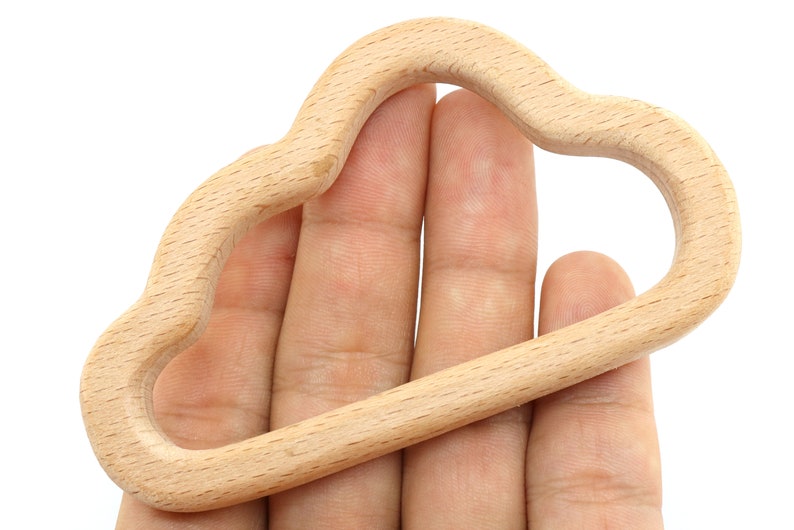 Puede incluir: Un anillo de dentici&oacute;n de madera natural con forma de nube. El anillo es liso y tiene un borde redondeado.