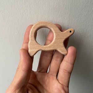 May include: A wooden turtle toy with a ring in the center. The toy is light brown and has a smooth finish.