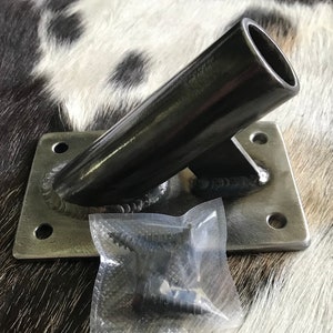 May include: A black metal wall mount with a square base and a curved arm. The mount is designed to hold a pole or rod. It comes with four screws in a clear plastic bag.