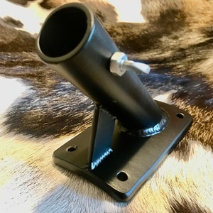 May include: A black metal bracket with a cylindrical opening angled upwards. The bracket has a rectangular base with four holes and a supporting arm. A silver bolt with a wing nut is attached to the cylindrical opening.