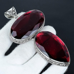 May include: A silver pendant with two large, faceted, red gemstones. The pendant has an ornate, filigree design.