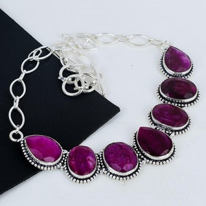 May include: A silver necklace with a chain and six teardrop-shaped pink gemstones. The gemstones are set in silver and have a faceted design.