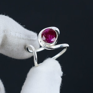 May include: A silver ring with a swirling design and a large, round, dark pink gemstone.