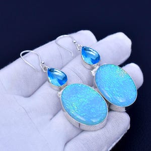 May include: A pair of silver dangle earrings with blue opal and blue topaz stones. The earrings have a teardrop-shaped blue topaz stone at the top and a larger oval-shaped blue opal stone at the bottom.