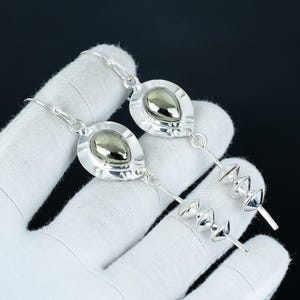 May include: Silver earrings with a teardrop-shaped pyrite stone set in a silver bezel. The earrings have a long, dangling design with multiple silver beads. The jewellery is displayed against a dark background.