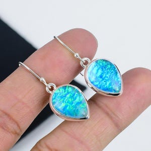 May include: A pair of silver teardrop earrings with blue opal stones. The earrings have a simple design and are perfect for everyday wear.