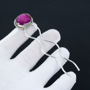 May include: Silver hair stick with a pink gemstone set in a silver bezel. The stick is wavy and has a decorative design.