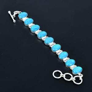 May include: A silver bracelet featuring oval-shaped, light blue gemstones. The gemstones are set in individual silver bezels and connected by silver links. The bracelet has a toggle clasp closure. The background is black.