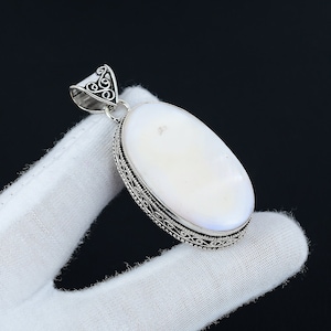 May include: A white oval pendant with a silver filigree design around the edge. The pendant is hanging from a silver bail.
