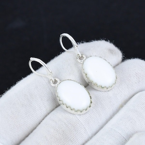 May include: A pair of silver dangle earrings with white oval-shaped stones. The stones have a scalloped edge.