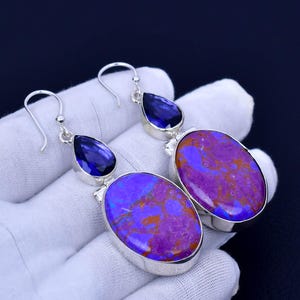 May include: A pair of dangle earrings with a purple and blue stone set in silver. The earrings feature a teardrop-shaped blue stone and a larger oval-shaped purple stone.