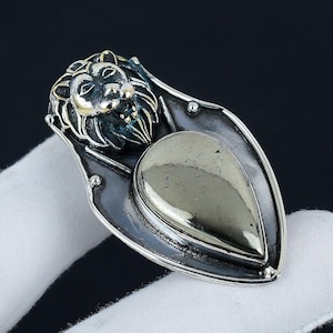 Puede incluir: Un colgante de plata con un diseño de cabeza de león y una piedra de pirita en forma de lágrima.