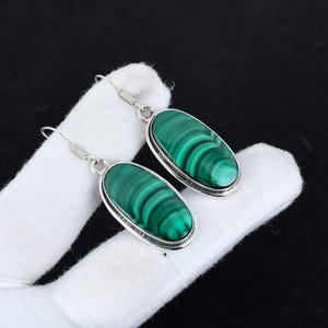 May include: A pair of silver earrings with oval-shaped green malachite stones. The stones have a swirling pattern.