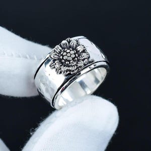 May include: A silver ring with a spinning sunflower design. The ring is textured and has a hammered finish.
