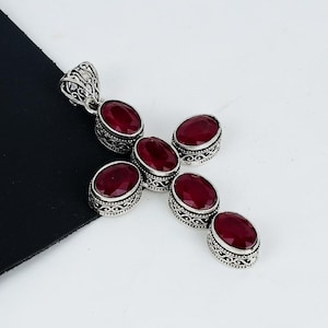 May include: Silver cross pendant featuring six oval-shaped red gemstones. The pendant has an intricate design with filigree details.