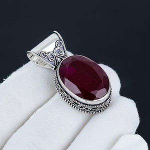 Puede incluir: Un colgante de plata con una piedra preciosa roja ovalada engastada en un marco de filigrana de plata.