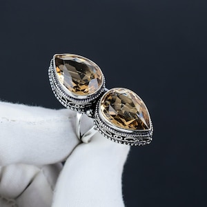 May include: A silver ring with two teardrop-shaped topaz gemstones. The ring has an ornate design with intricate details.