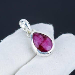 Könnte beinhalten: Ein silberner Anhänger mit einem tropfenförmigen Rubin-Edelstein. Der Rubin ist tiefrosa und hat einen facettierten Schliff.