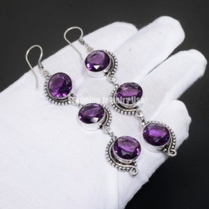 May include: A pair of silver dangle earrings with multiple round amethyst gemstones. The earrings have a hook closure.