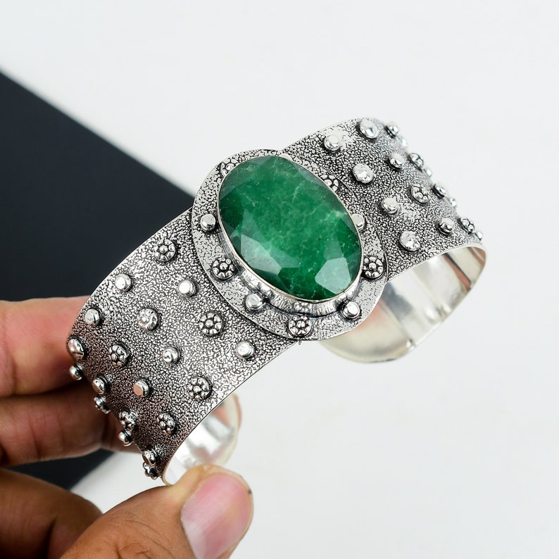 May include: A silver cuff bracelet with a large, oval-shaped green gemstone set in a decorative silver bezel. The bracelet has a textured surface with small, raised dots.