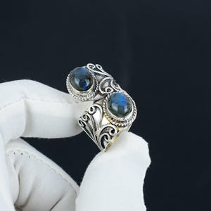 Puede incluir: Un anillo de plata con dos piedras ovaladas de labradorita azul engastadas en un diseño ornamentado y en espiral.