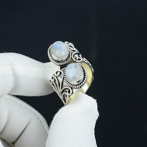 Op de afbeelding: Een zilveren ring met twee ovale maansteen edelstenen gezet in een decoratief filigraan ontwerp.