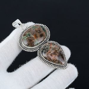 May include: A silver pendant with two teardrop-shaped green and brown agate stones set in a beaded silver frame.