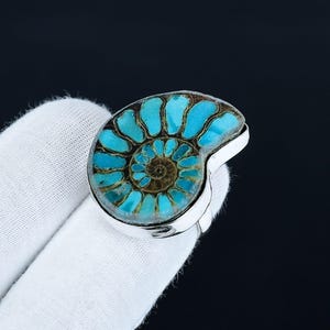 Peut inclure: Bague en argent ornée d'un fossile d'ammonite. Le fossile présente un motif en spirale aux teintes turquoise et marron. La bague est montée sur un anneau en argent poli. Bijou unique.