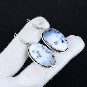 May include: A pair of silver earrings with oval-shaped dendritic opal stones. The stones are white with black dendritic patterns.