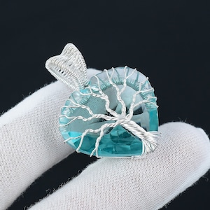 May include: A silver wire wrapped heart-shaped pendant with a blue crystal and a tree design.