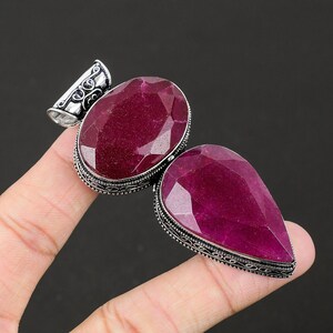 May include: A silver pendant with two large, faceted, ruby red gemstones. The pendant has an ornate, filigree design.