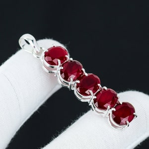 May include: A silver pendant with six red oval gemstones set in a row. The pendant is on a white surface.