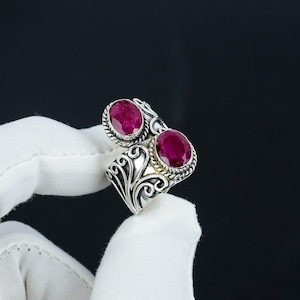 May include: A silver ring with two oval-shaped ruby gemstones set in a decorative floral design.