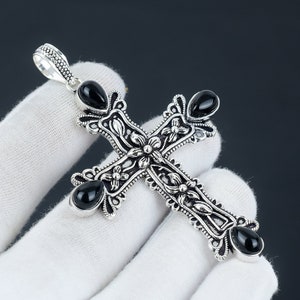 May include: A silver cross pendant with black onyx stones set in the center of each arm. The cross is intricately detailed with floral designs.