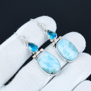 May include: A pair of silver dangle earrings with oval shaped blue and white gemstone drops. The earrings have a teardrop shaped blue gemstone at the top of each drop.