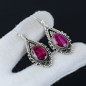 May include: A pair of silver dangle earrings with a pink gemstone set in each. The earrings have a detailed design with small beads around the gemstone.
