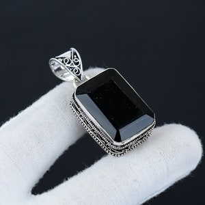 Puede incluir: Un colgante de plata con una piedra preciosa negra engastada en un marco decorativo. El colgante tiene un diseño de filigrana y es perfecto para agregar un toque de elegancia a cualquier atuendo.