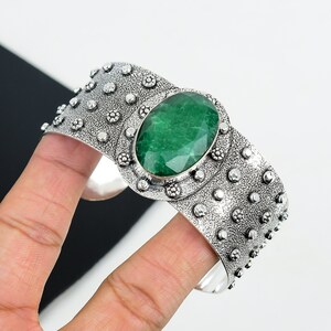 May include: A silver cuff bracelet with a large, oval-shaped green gemstone set in a decorative silver bezel. The bracelet has a textured surface with small, raised dots.