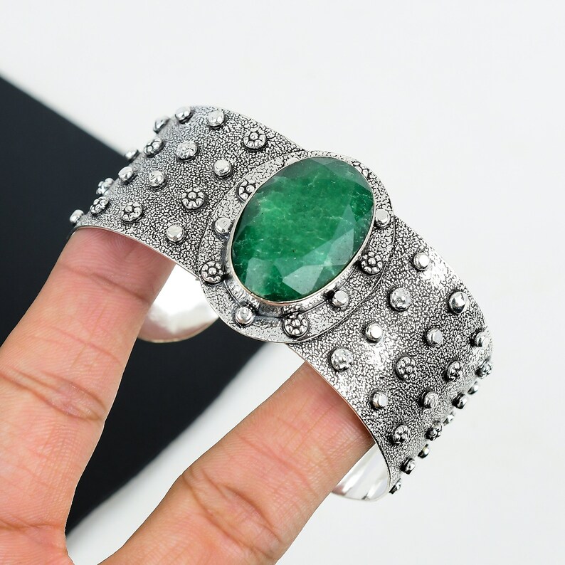 May include: A silver cuff bracelet with a large, oval-shaped green gemstone set in a decorative silver bezel. The bracelet has a textured surface with small, raised dots.