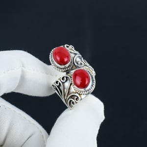 May include: A silver ring with two red oval-shaped stones set in ornate silver settings. The ring is open and adjustable.