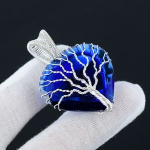 Könnte beinhalten: Ein Anhänger aus Silberdraht in Form eines Lebensbaums mit einem blauen herzförmigen Kristall.