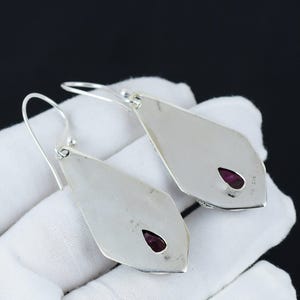 Peut inclure: Une paire de boucles d'oreilles pendantes en argent avec une pierre pr&eacute;cieuse violette en forme de larme sertie dans chaque boucle d'oreille.