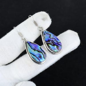 May include: A pair of silver teardrop earrings with iridescent abalone shell inlays. The earrings have a silver hook closure.